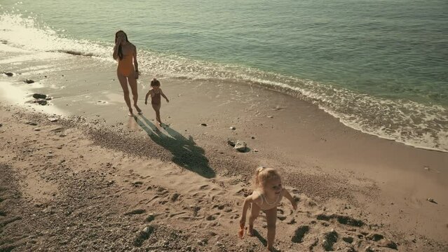 Aerial slow motion clip, mother and her little girls spend vacation on the sea beach together