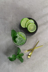 top view Mojito drink with ice cubes in glass, limes, kiwi and mint leaves on grey background on a rooftop bar