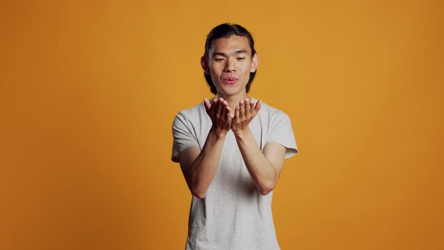 Male model blowing air kisses in studio, acting silly and sensual on orange backdrop. Carefree man sending kisses and being flirty, acting romantic with kissy funny face. Natural confidence.