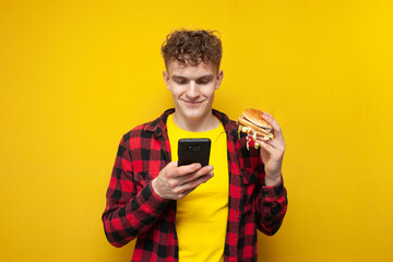 curly guy holds a big burger and uses a smartphone, a student eats fast food and looks into the...