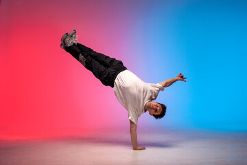 dancer doing acrobatic trick and dancing breakdance in neon red and blue lighting, young guy stands on his hands