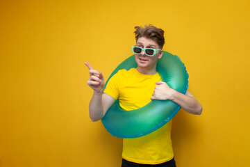 young guy with a swimming inflatable ring points his finger to the side on a yellow background