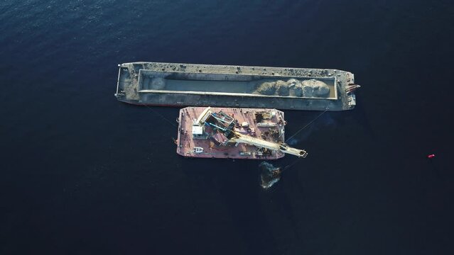 Aerial view. The dredger is working. Extraction of river sand by a special floating crane. A dredging machine takes sand from the bottom of the river and loads it onto a barge. Top view.