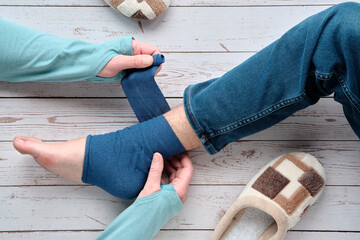 An adult wrapping compression bandage around sprained ankle of teenage boy to reduce ache. Feet...