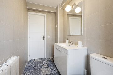Bathroom with white lacquered furniture with a white resin countertop, hydraulic tiles and a frameless square mirror on the wall