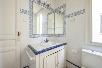 Bathroom with vintage style white tiles with blue borders and blue patterned borders surrounding the mirror and brass taps