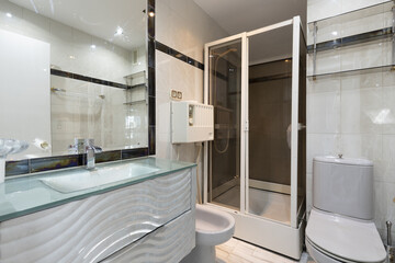 Bathroom with white lacquered furniture with tempered glass top, built-in wall mirror and square shower cabin with screens