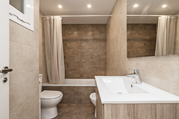 Small bathroom with a one-piece resin sink on oak furniture with drawers, a bathtub with a white plastic curtain and porcelain toilets