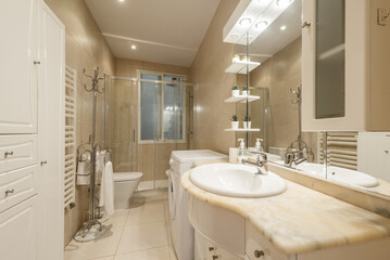 Bathroom with cream marble sink with wooden cabinet with integrated mirror with lights and shelves and washing machine in one corner