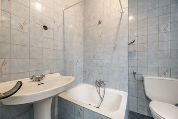Vintage well-worn bathroom with blue tiles, small bathtub and white toilets