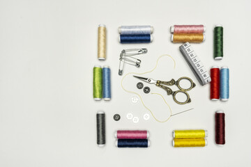 Sewing still life with spools of colored threads, buttons, metal scissors, tape measure and needle on a white background.