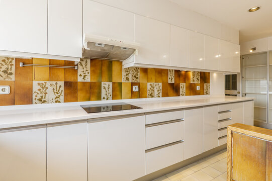 elongated kitchen with smooth white cabinets, white faux stone countertops, orange outdated tiles and light flooring