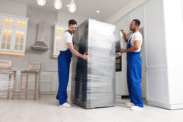 Male movers with stretch film wrapping refrigerator in new house