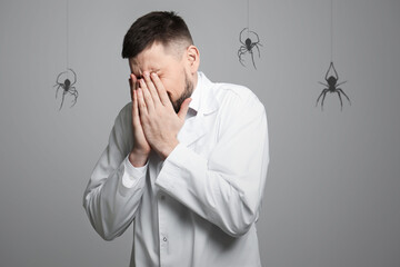 Scared man suffering from panic attack on grey background. Shadows of spiders symbolizing fear and...
