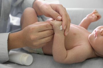 Obraz na płótnie Canvas Mother applying moisturizing cream onto baby`s hand on changing table, closeup