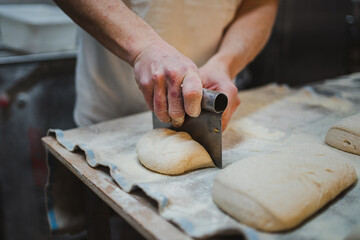 Baker man dividing fresh bread dough with steel scraper in a bakery