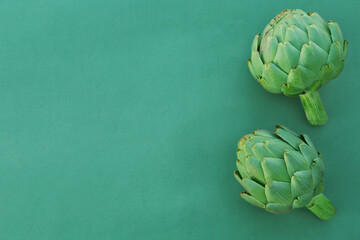 Whole fresh raw artichokes on green background, flat lay. Space for text