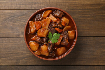 Delicious beef stew with carrots, parsley and potatoes on wooden table, top view