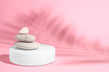 Obraz na płótnie Canvas Cosmetic product, stacked stones and shadow of tropical leaf on pink background. Space for text