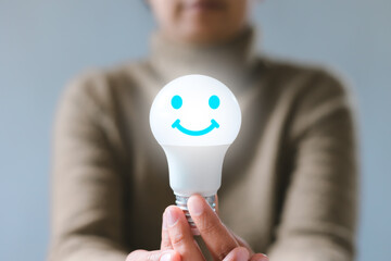 Hand holding a light bulb with smiley face icon. Satisfaction survey and customer service concept....