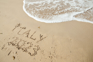 Italy 2023 lettering on the beach with wave and clear blue sea. 