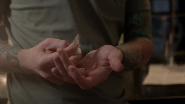 Close up view, young guy with tattoos on his arms takes pill from blister and puts it in his palm. man is going to take pill, take medicine in morning or evening in kitchen.