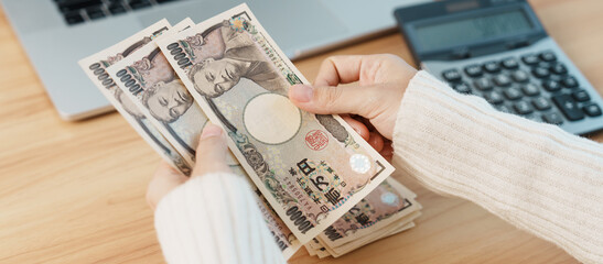 Woman hand counting Japanese Yen banknote with calculator. Thousand Yen money. Japan cash, Tax,...