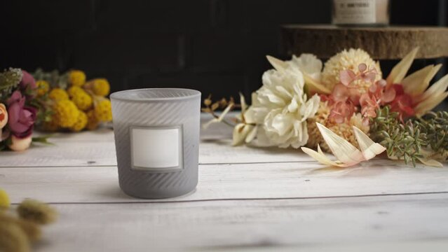 Candle on a white wooden table with a black brick wall. Moving from right to left on a packshot of a candle with a white lable to track and add your information or logo.