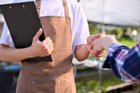 Cropped image of a hydroponic farm owner shaking hands with a supplier in the greenhouse