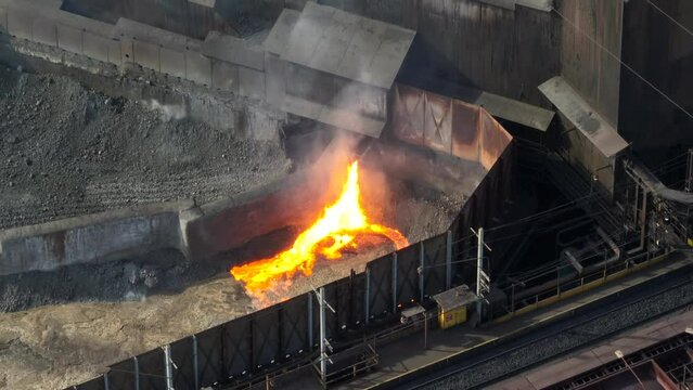 Hot molten steel spewing from USS steel mill building. Long aerial zoom of unsafe practices and environmental, climate change issues.