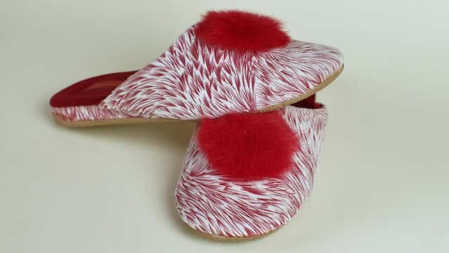 Female house slippers with beautiful motley red and white pattern with bright red pompom. Pair of female slippers for house. Modern indoor shoes for walking around house, soft, warm and comfortable
