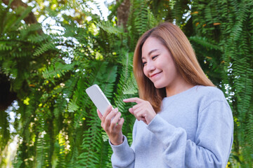 Portrait image of a beautiful young asian woman holding and using mobile phone in the outdoors
