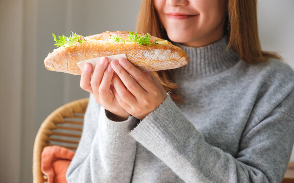 Closeup image of a young woman holding a piece of french baguette sandwich at home