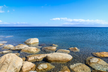 Beautiful Sayram Lake natural scenery in Xinjiang, China. Clear lake water and rocks under blue sky.