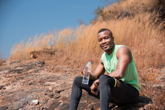 African American athletic man resting on the way sitting drinking water after running sport training outdoor in summer, workouts running and healthy lifestyle, sports and wellness.
