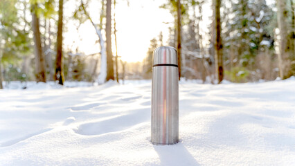 Metal thermos with a hot drink on the background of a winter mountain waterfall. Insulated drink container in the snow