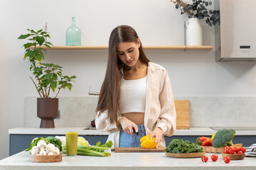 An attractive woman cuts vegetables for a salad, standing at the kitchen table. Healthy eating