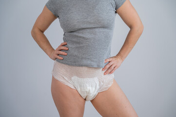 Woman in adult diapers and gray t-shirt on a white background. Incontinence problem.
