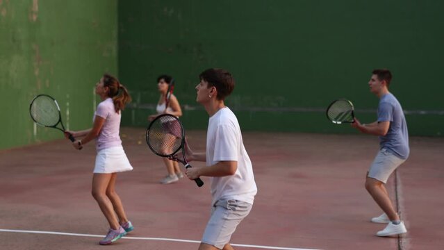 Group of sporty young frontenis player swinging string racquet to hit ball on outdoor walled court on sunny summer day. Sport and active lifestyle concept