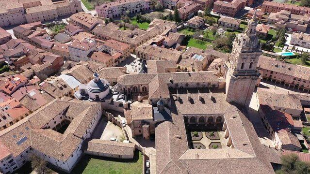 Drone view of Spanish town of El Burgo de Osma in spring overlooking traditional terracotta tiled roofs of residential buildings surrounded by green hills and medieval Roman Catholic gothic cathedral