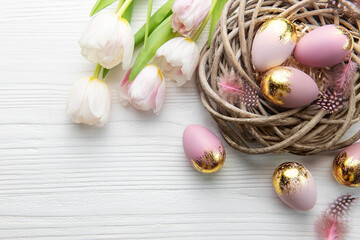 Nest with Easter eggs painted pink and golden colors on a white wooden background.