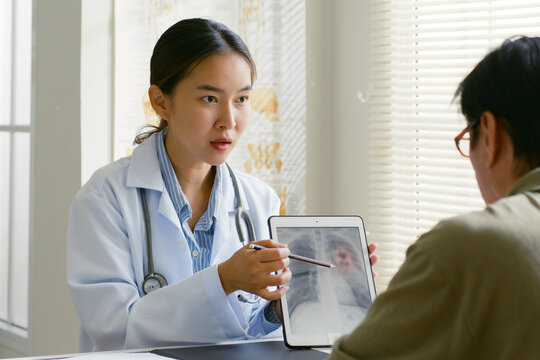 Young Asian woman doctor showing lung x-ray test results and describe to a senior patient in hospital. For cancer awareness month