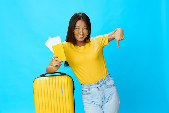 Asian woman traveling with yellow suitcase and tickets with passport in hand, tourist traveling by plane and train with luggage on blue background