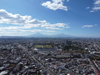 a drone photo aerial view of the city in puebla, mexico, hispanic downtown with the blue sky, clouds and travel, with the university and two volcanoes in the background 