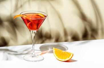 Martinez alcoholic cocktail drink with red vermouth, liqueur, orange bitter, zest and ice. Light beige background, hard light, shadow pattern - obrazy, fototapety, plakaty