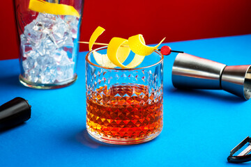 Sazerac cocktail with cognac, bourbon, absinthe, bitters, sugar and lemon zest. Dazzling red blue background with hard light and harsh shadows