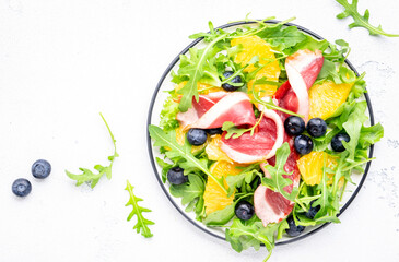 Gourmet salad with smoked duck, oranges, blueberries, arugula and lettuce, white table background, top view