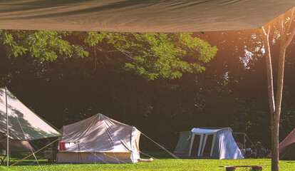 View from under sunshade canvas of Field Tents and Travelers group Relaxing in the shade of trees on green lawn in Campground area at natural parkland