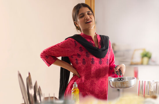 Woman suffering from back pain while washing dishes in kitchen