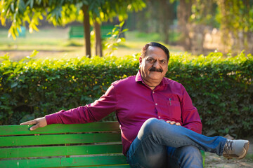 Naklejka na ściany i meble Indian man relaxing on bench in park.